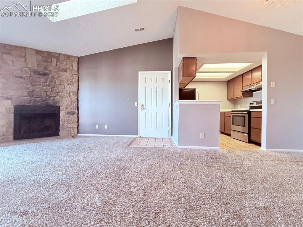 Image 6 of 35: Unfurnished living room featuring vaulted ceiling, a skylight, light carpet