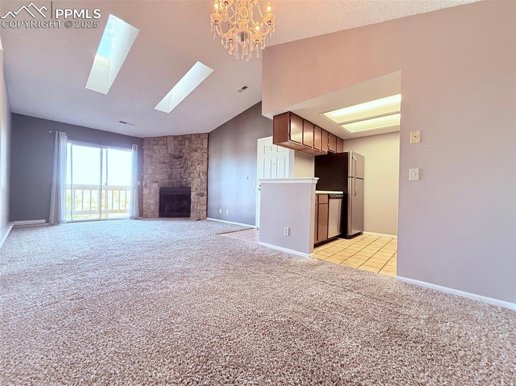 Image 9 of 35: Unfurnished living room featuring light carpet, vaulted ceiling, a fireplac