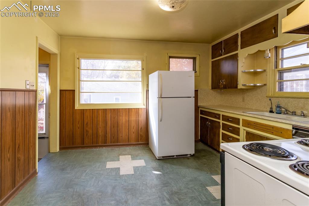 Image 10 of 24: Kitchen with wood walls, white appliances, light countertops, open shelves,
