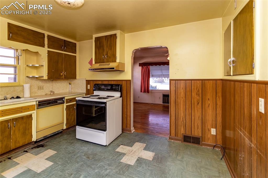 Image 11 of 24: Kitchen with wainscoting, wood walls, white electric range, light counterto