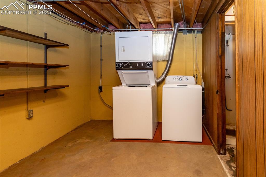 Image 14 of 24: Laundry area with unfinished concrete floors and estacked washer and dryer