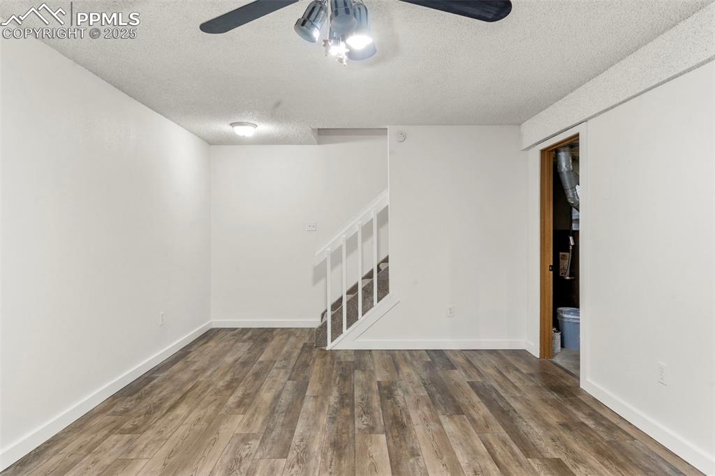 Image 21 of 24: Empty room with stairway, wood finished floors, a textured ceiling, and cei