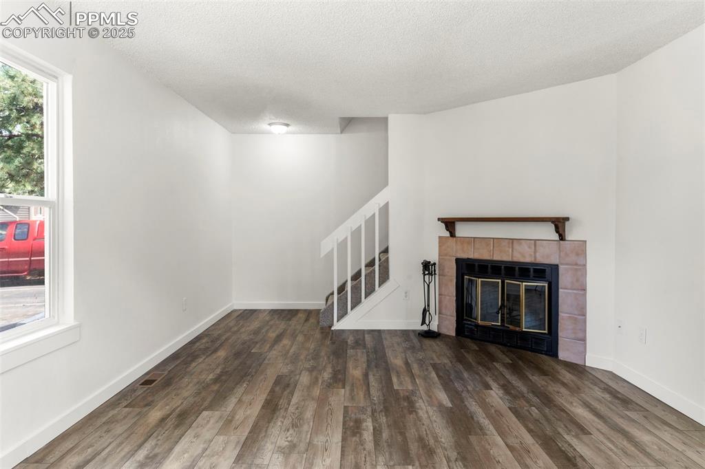 Image 4 of 24: Unfurnished living room featuring stairway, dark wood-style flooring, a til
