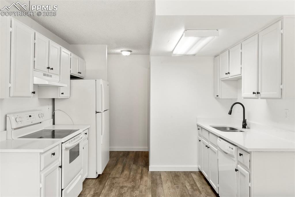 Image 7 of 24: Kitchen featuring white appliances, dark wood-type flooring, white cabinets