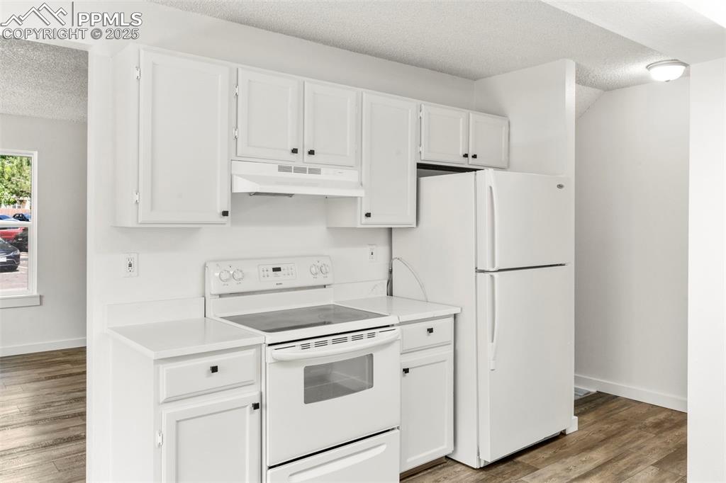 Image 8 of 24: Kitchen with white appliances, a textured ceiling, white cabinetry, light w