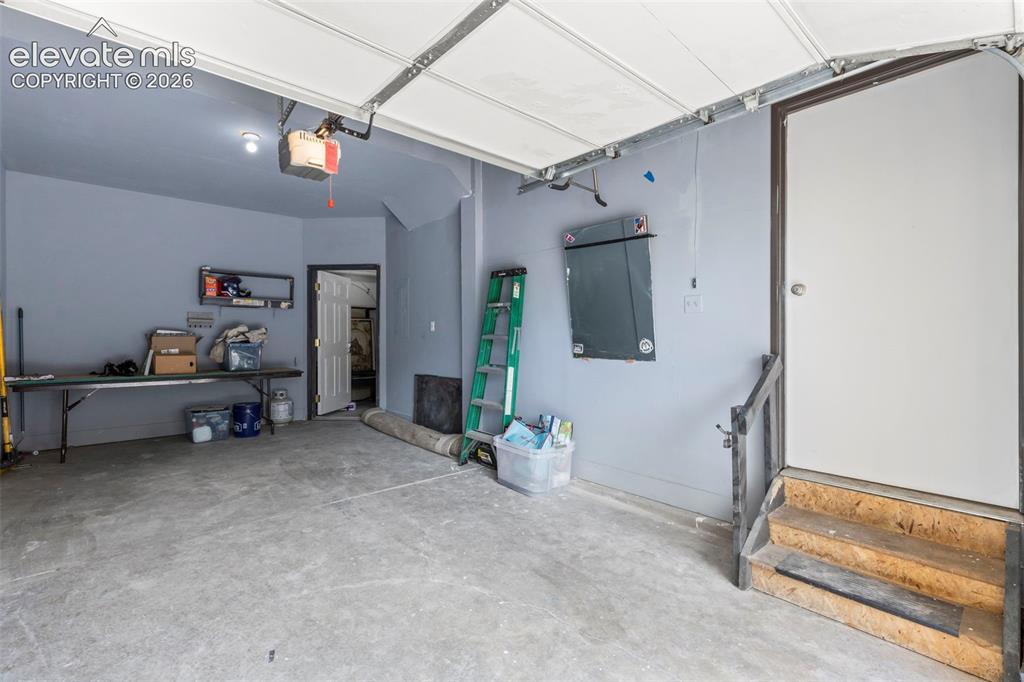 Image 18 of 22: Concrete floor garage with a white overhead door and an internal access doo