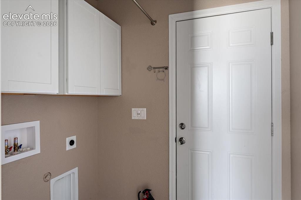 Image 12 of 21: Utility area featuring a paneled door, white upper cabinetry, and laundry h