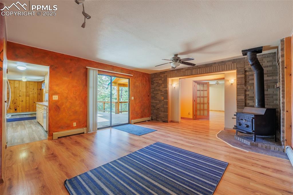 Image 12 of 32: Unfurnished living room featuring baseboard heating, a wood stove, light wo