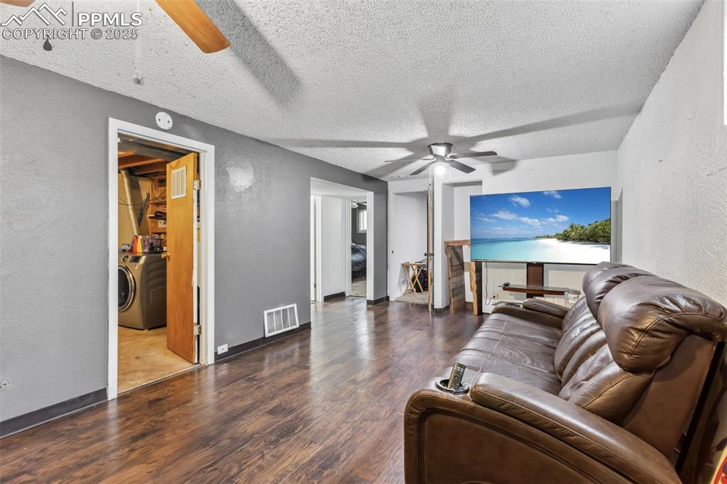 Image 17 of 20: Living area with ceiling fan, washer / dryer, a textured wall, wood finishe