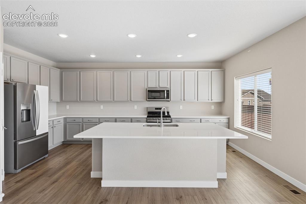Image 10 of 40: Kitchen featuring light-toned cabinetry, quartz countertops, a central isla