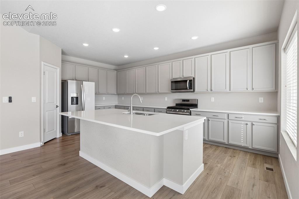 Image 9 of 40: Kitchen featuring light gray cabinetry, a central island with a quartz coun