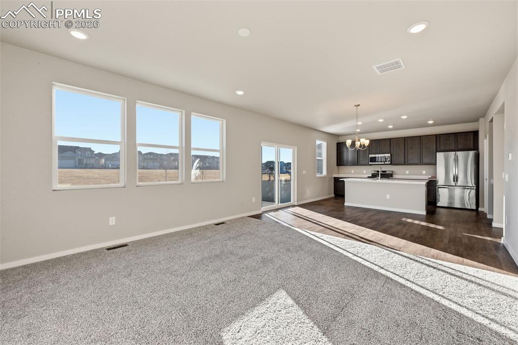 Image 10 of 48: Unfurnished living room with a chandelier and dark colored carpet