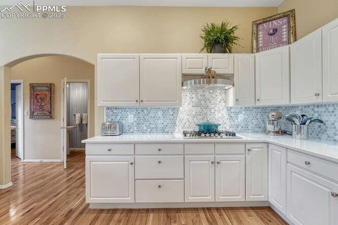 Image 18 of 48: Kitchen featuring white cabinets, light wood-style floors, arched walkways,
