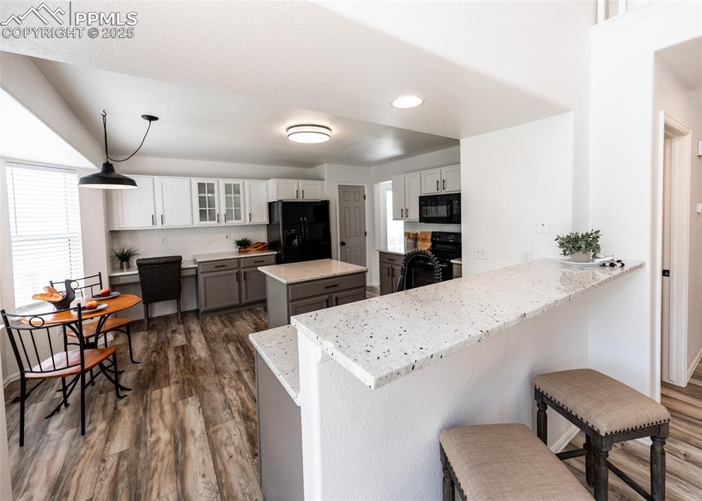 Image 12 of 50: Kitchen featuring black appliances, a breakfast bar, dark wood-type floorin