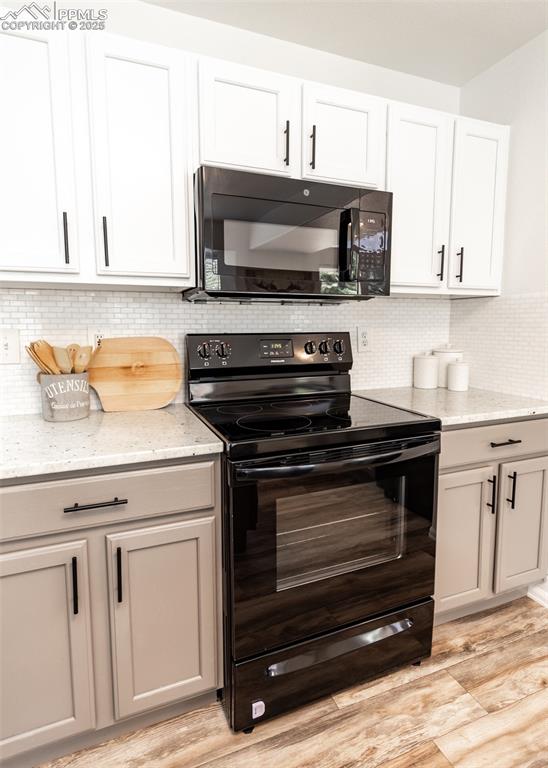 Image 14 of 50: Kitchen featuring black appliances, light wood-type flooring, light stone c