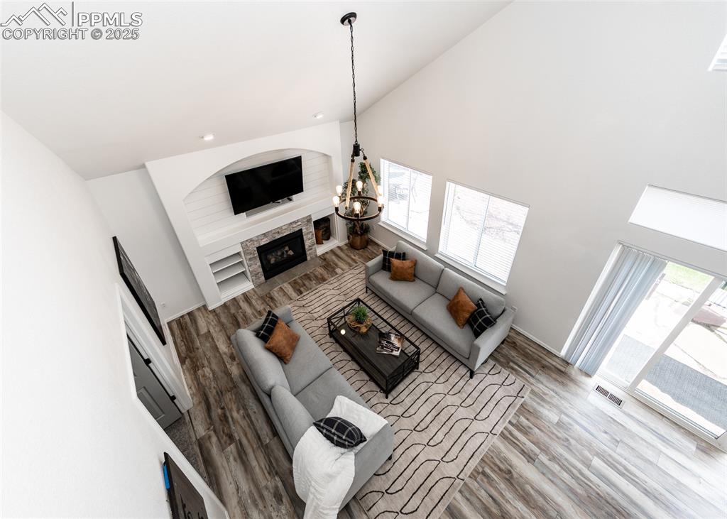 Image 20 of 50: Living room with wood finished floors, a fireplace, a chandelier, high vaul