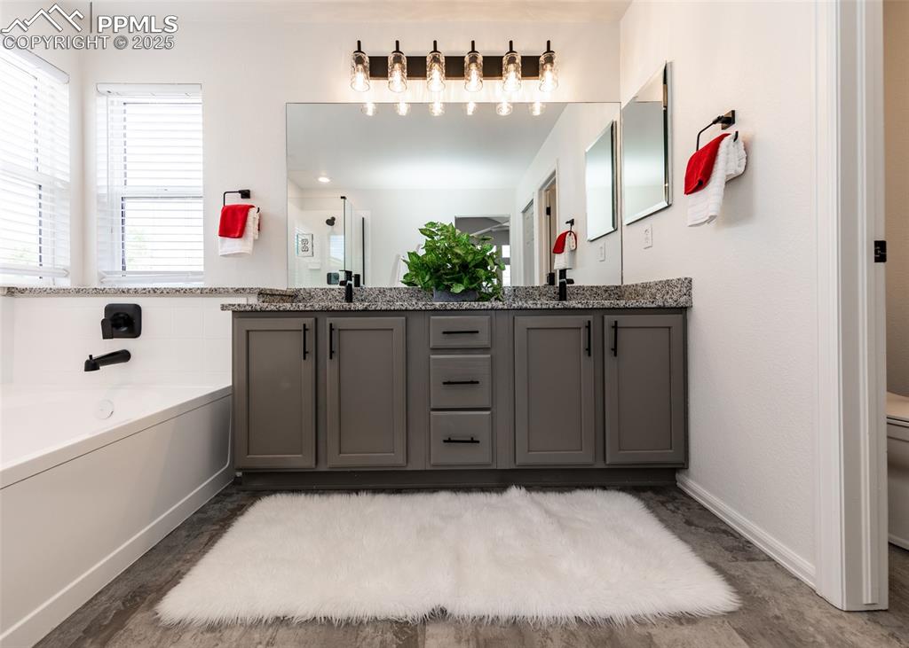 Image 37 of 50: Bathroom featuring a garden tub, double vanity, baseboards, and wood finish