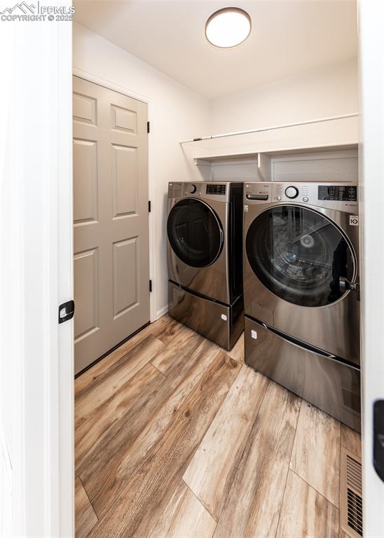 Image 45 of 50: Clothes washing area with washer and clothes dryer and wood finished floors