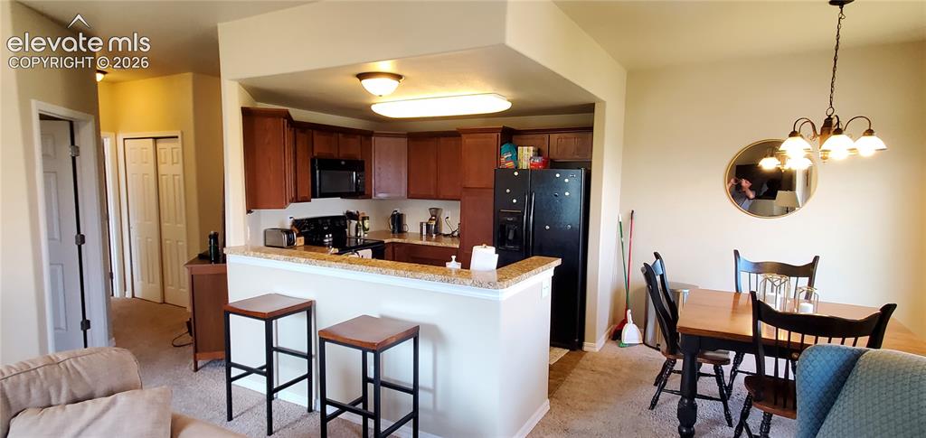 Image 5 of 20: Kitchen with wood-finish cabinetry, black appliances, and a light-toned cou