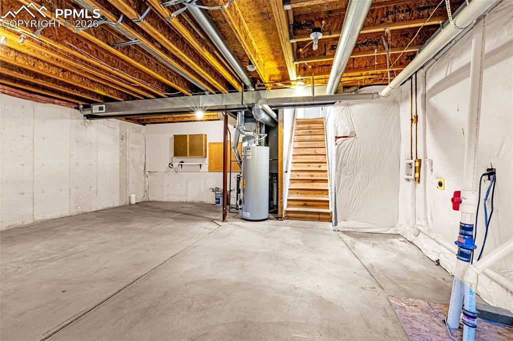 Image 24 of 28: Unfinished below grade area featuring stairs and gas water heater