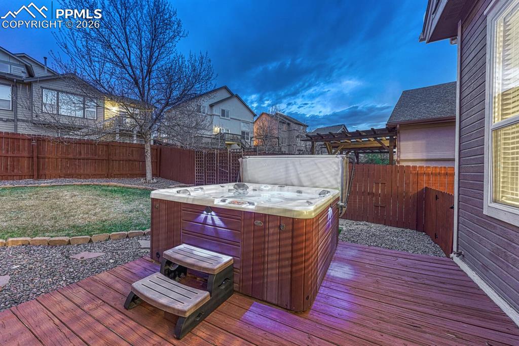 Image 45 of 50: Fenced backyard with deck, pergola, and hot tub.