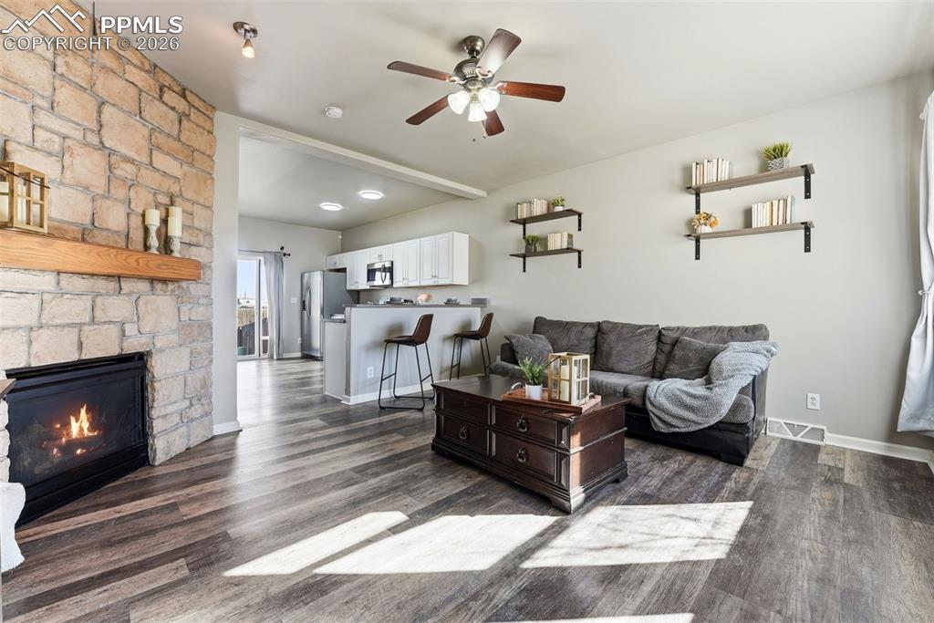 Image 4 of 41: Living area with a ceiling fan, dark wood-type flooring, and a stone firepl