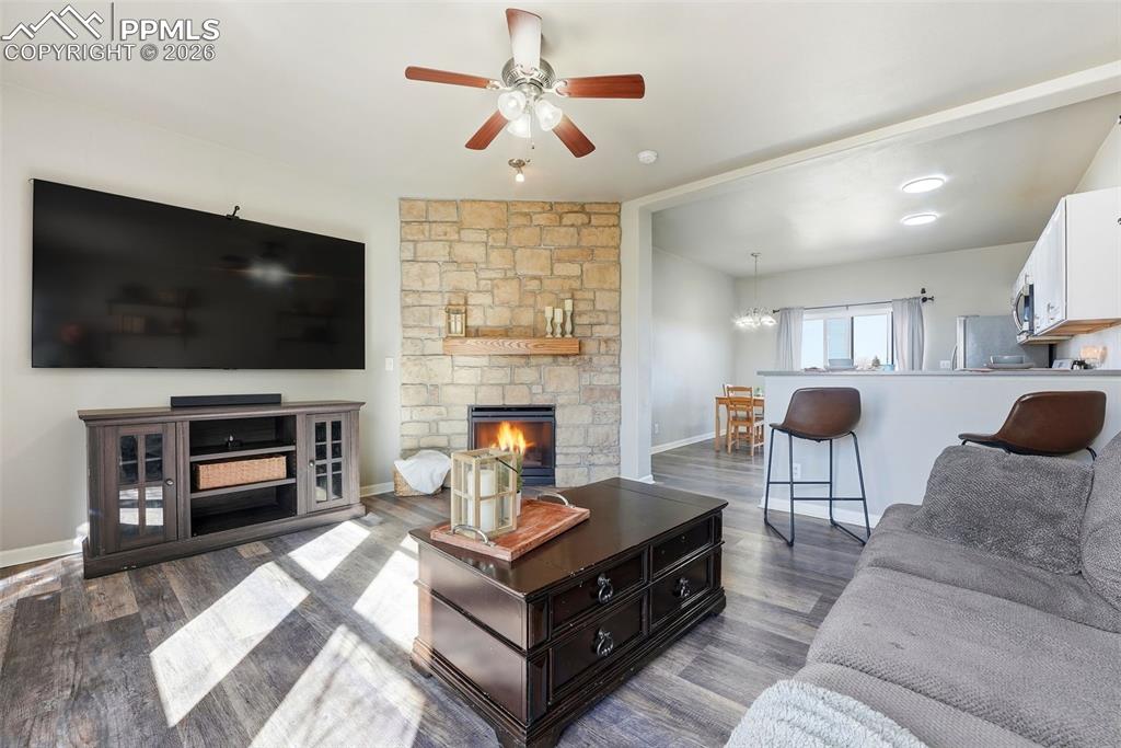 Image 5 of 41: Living room with ceiling fan, a stone fireplace, and dark wood-type floorin