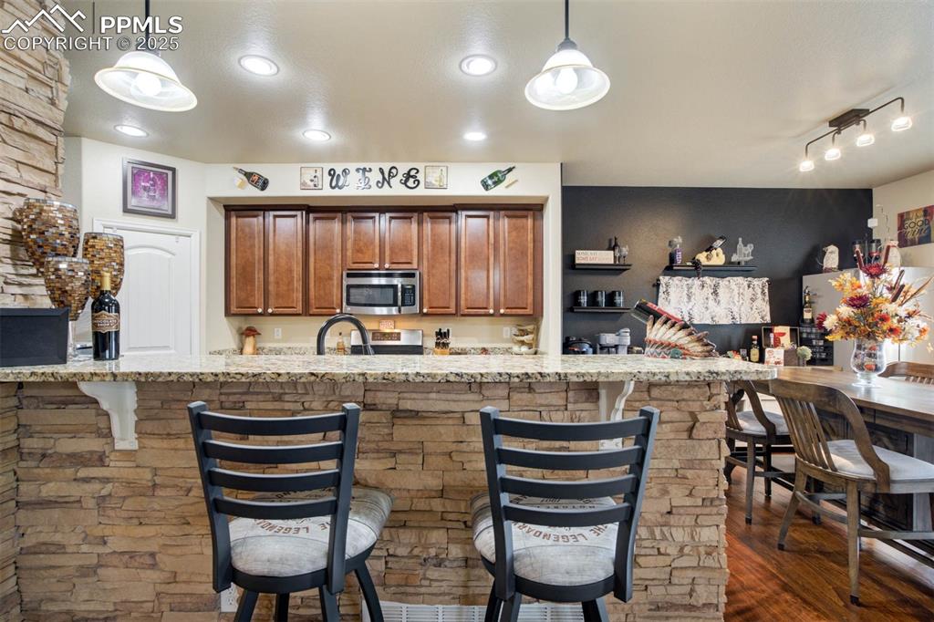 Image 11 of 49: Kitchen featuring stainless steel appliances, a breakfast bar, brown cabine