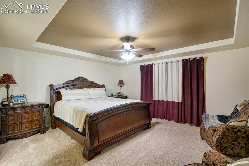 Image 21 of 49: Bedroom featuring a raised ceiling, carpet floors, and a ceiling fan
