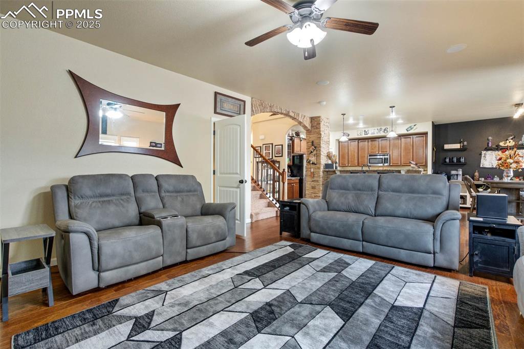 Image 8 of 49: Living room featuring ceiling fan, arched walkways, stairway, and wood fini