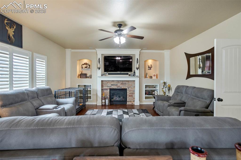 Image 9 of 49: Living area featuring wood finished floors, a ceiling fan, a stone fireplac