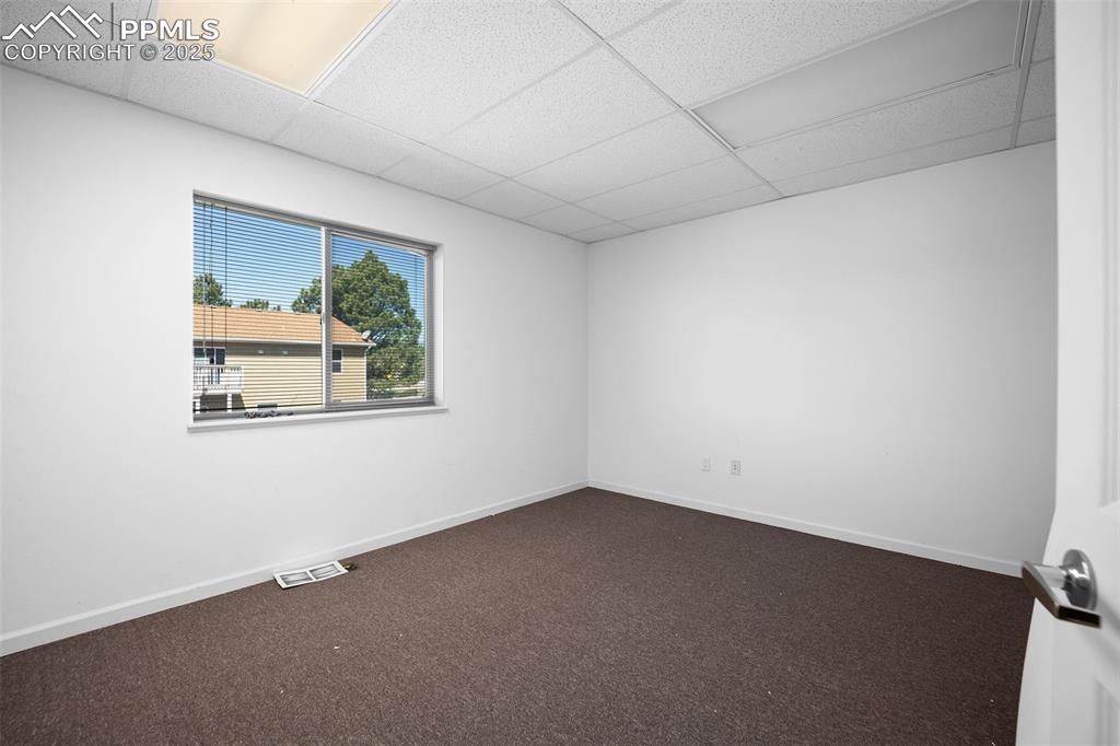 Image 16 of 50: Spare room with a paneled ceiling, dark carpet, and baseboards-5785 Buildin