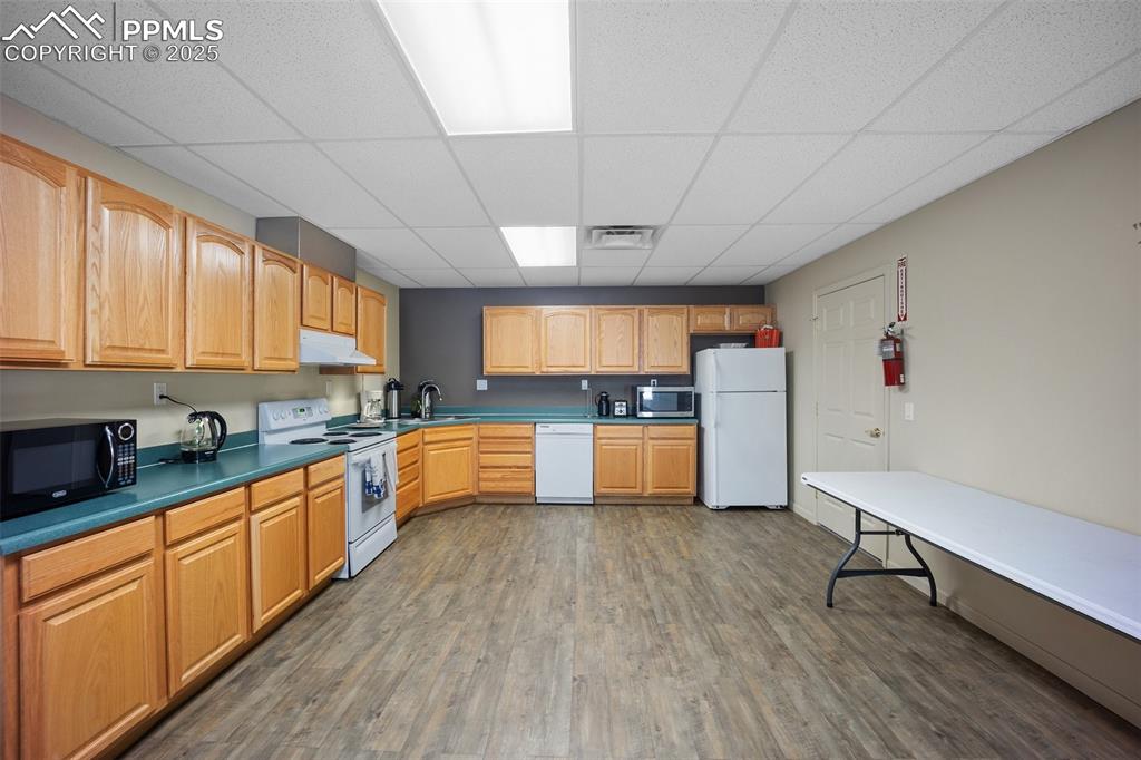 Image 36 of 50: Kitchen with white appliances, under cabinet range hood, a paneled ceiling,