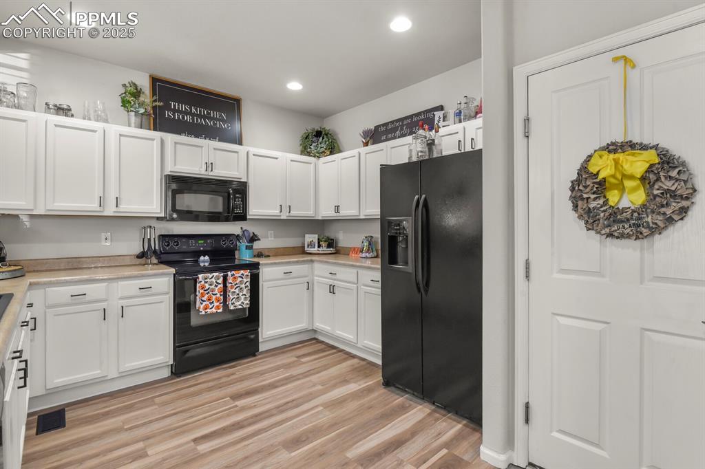 Image 14 of 27: Kitchen featuring black appliances, white cabinetry, light wood finished fl