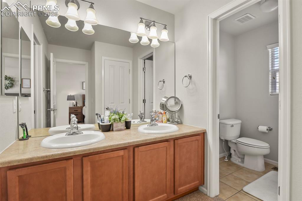 Image 18 of 27: Full bath with light tile patterned flooring, double vanity, and a chandeli