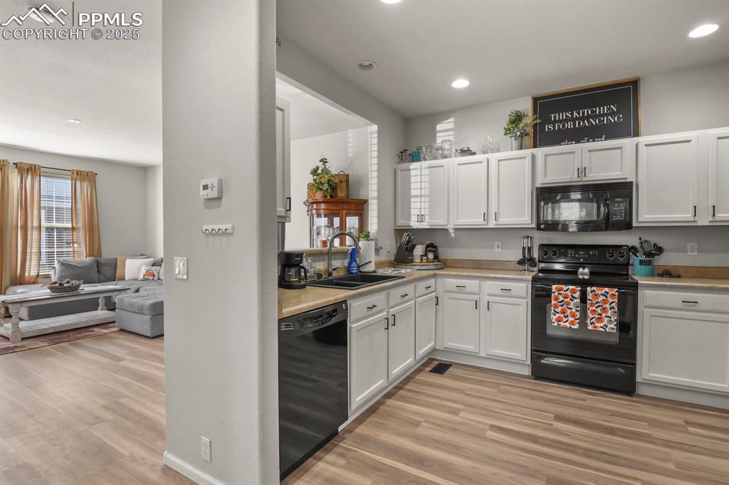 Image 9 of 27: Kitchen with black appliances, light wood finished floors, light countertop