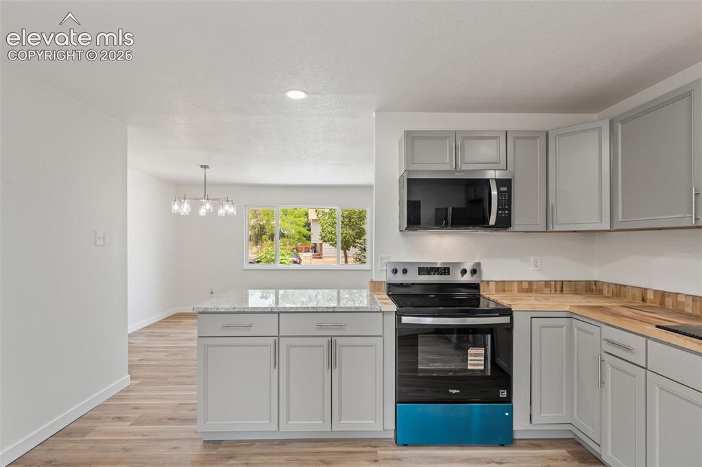 Image 14 of 35: Modern kitchen featuring light gray cabinetry, wood-finish countertops, sta