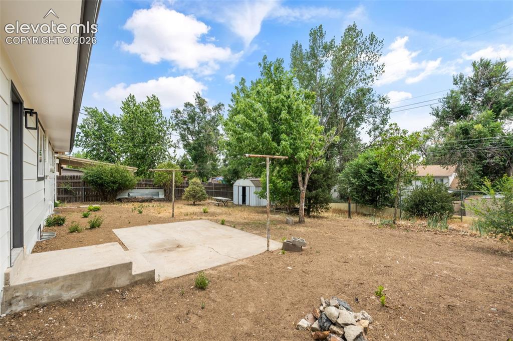 Image 34 of 35: Expansive backyard featuring a concrete patio, mature trees, a storage shed