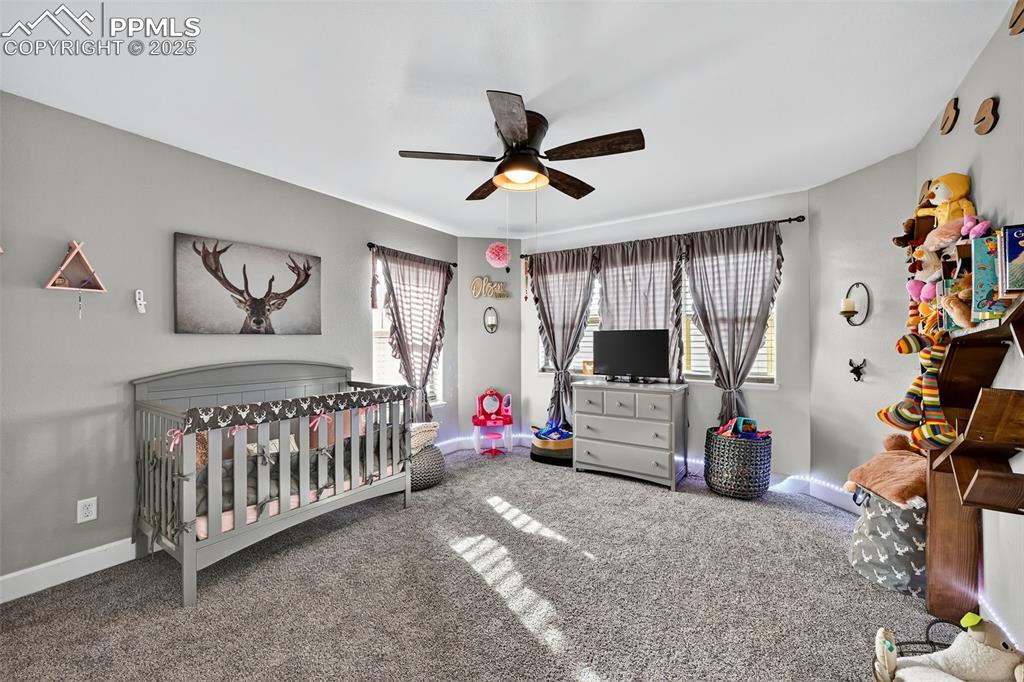 Image 21 of 39: Bedroom featuring a crib, carpet, and ceiling fan