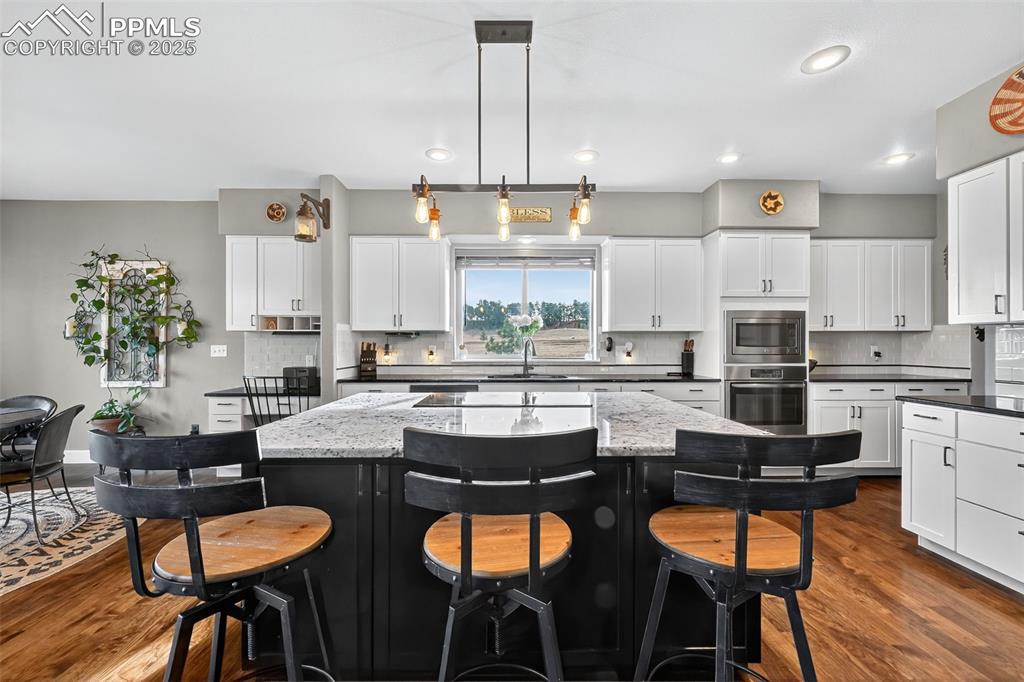 Image 7 of 39: Kitchen featuring dark cabinetry, a kitchen breakfast bar, dark wood-type f