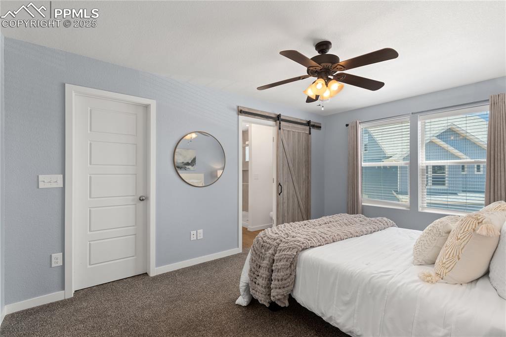 Image 16 of 33: Bedroom with a barn door, carpet flooring, and ceiling fan