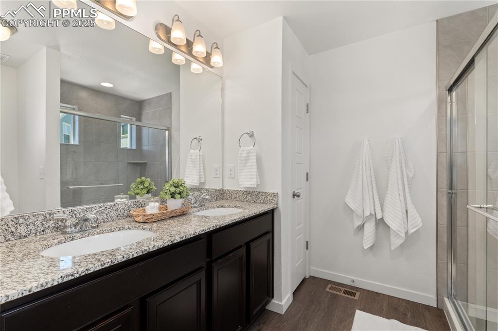 Image 18 of 33: Full bathroom with double vanity, wood finished floors, and a shower stall