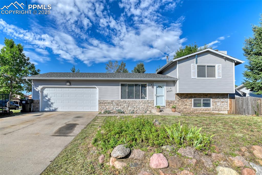 Caption: Split level home featuring stone siding, concrete driveway, an attached garage, and a shingled roof