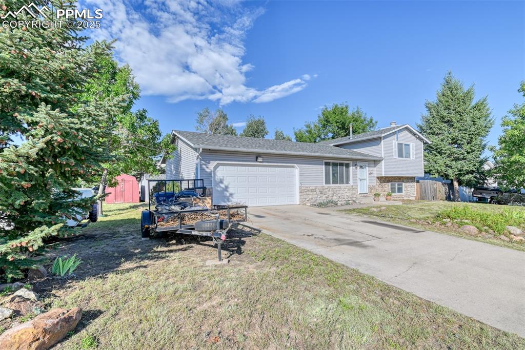 Image 2 of 38: Tri-level home with stone siding, an attached garage, and driveway