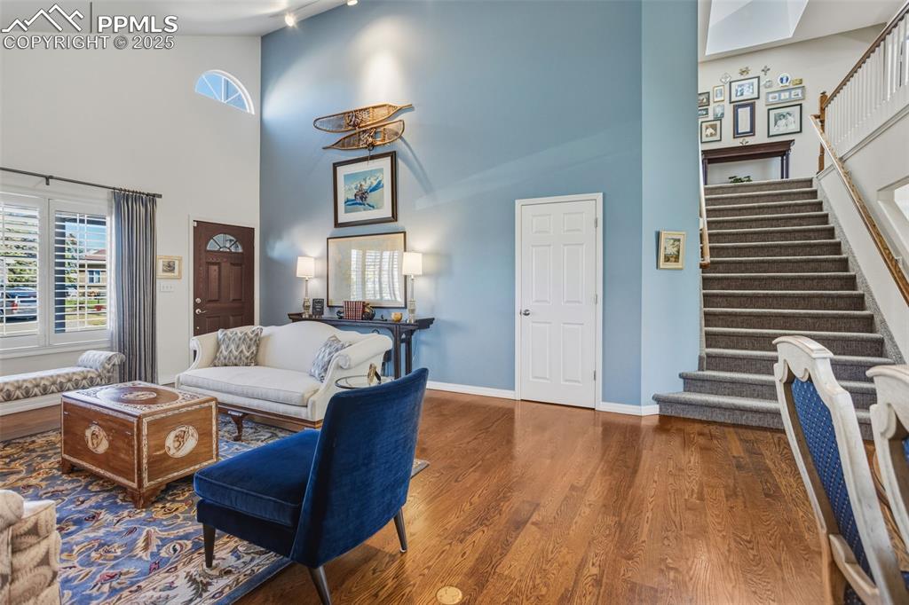Image 14 of 43: Living area with high vaulted ceiling, wood finished floors, and stairway