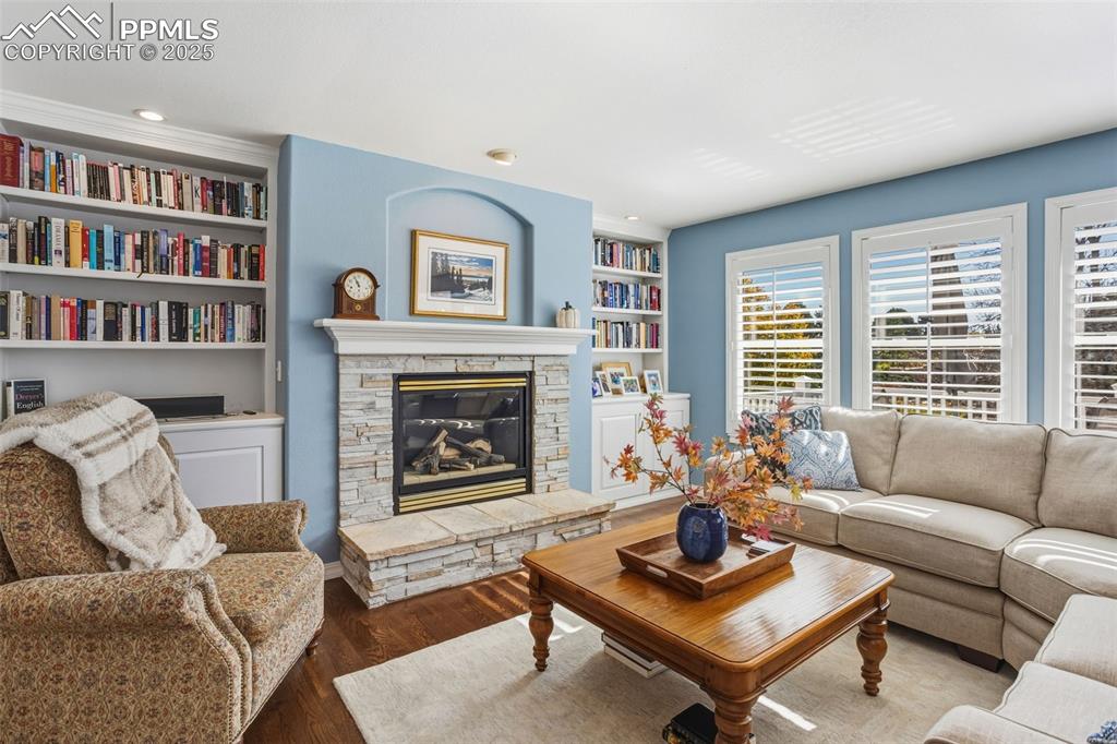 Image 22 of 43: Living room with dark wood-type flooring, a stone fireplace, built in shelv