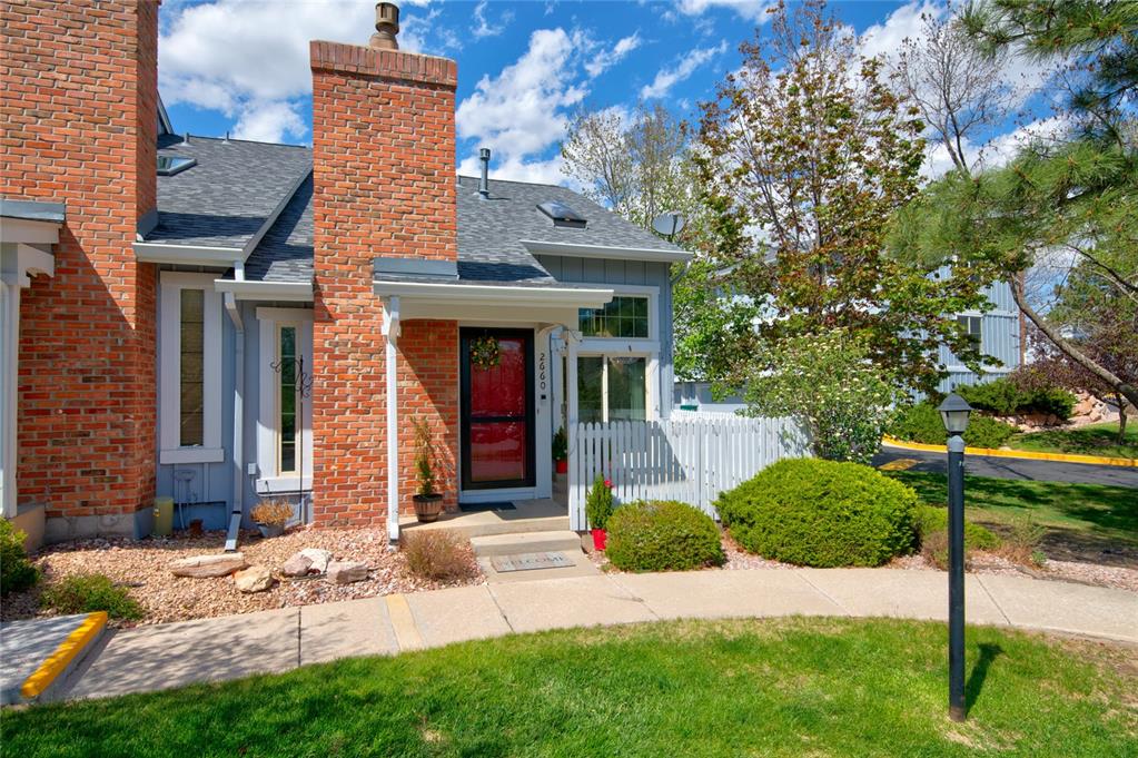 Caption: Brick and siding exterior featuring a red entry door, white picket fence, mature landscaping, and a 