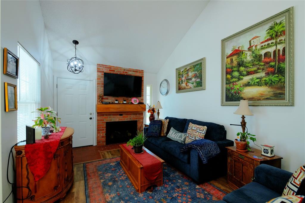 Image 4 of 21: Living area featuring a brick fireplace with a wood mantle, vaulted ceiling