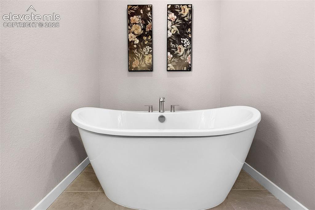 Image 22 of 36: Freestanding soaking tub with a deck-mounted faucet and tiled flooring