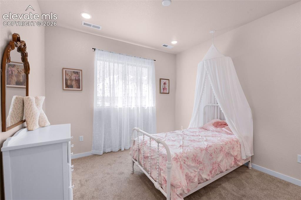 Image 25 of 36: Recessed lighting, light-toned carpeting, and a window with sheer white cur